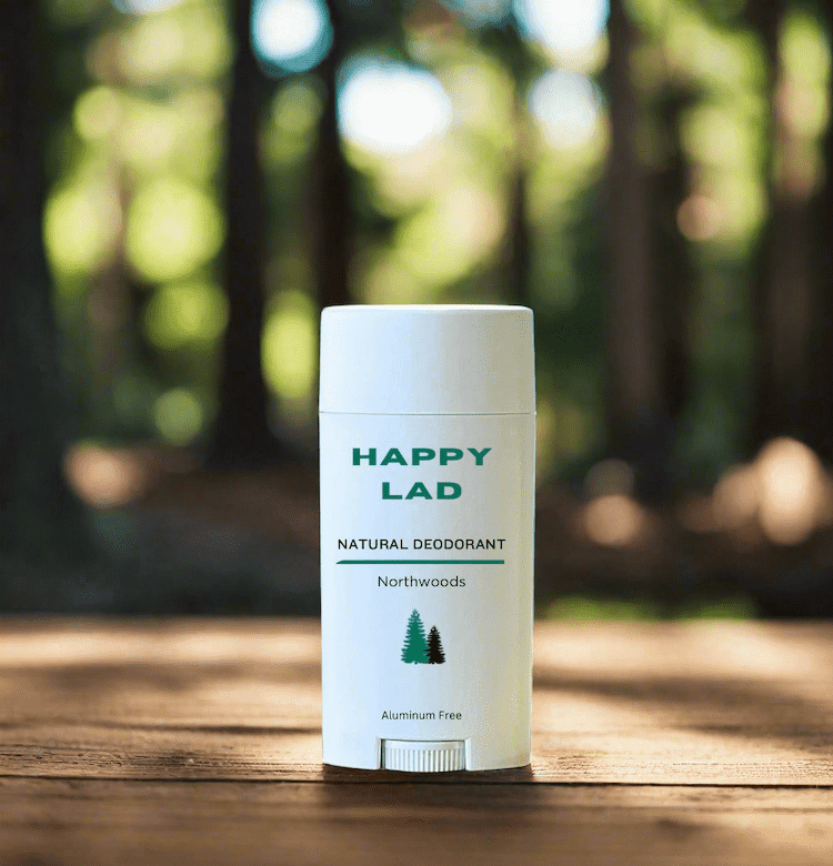 Northwoods essential oils scented natural deodorant for men from Happy Lad. Sitting on wood table with Northwoods trees in the background.