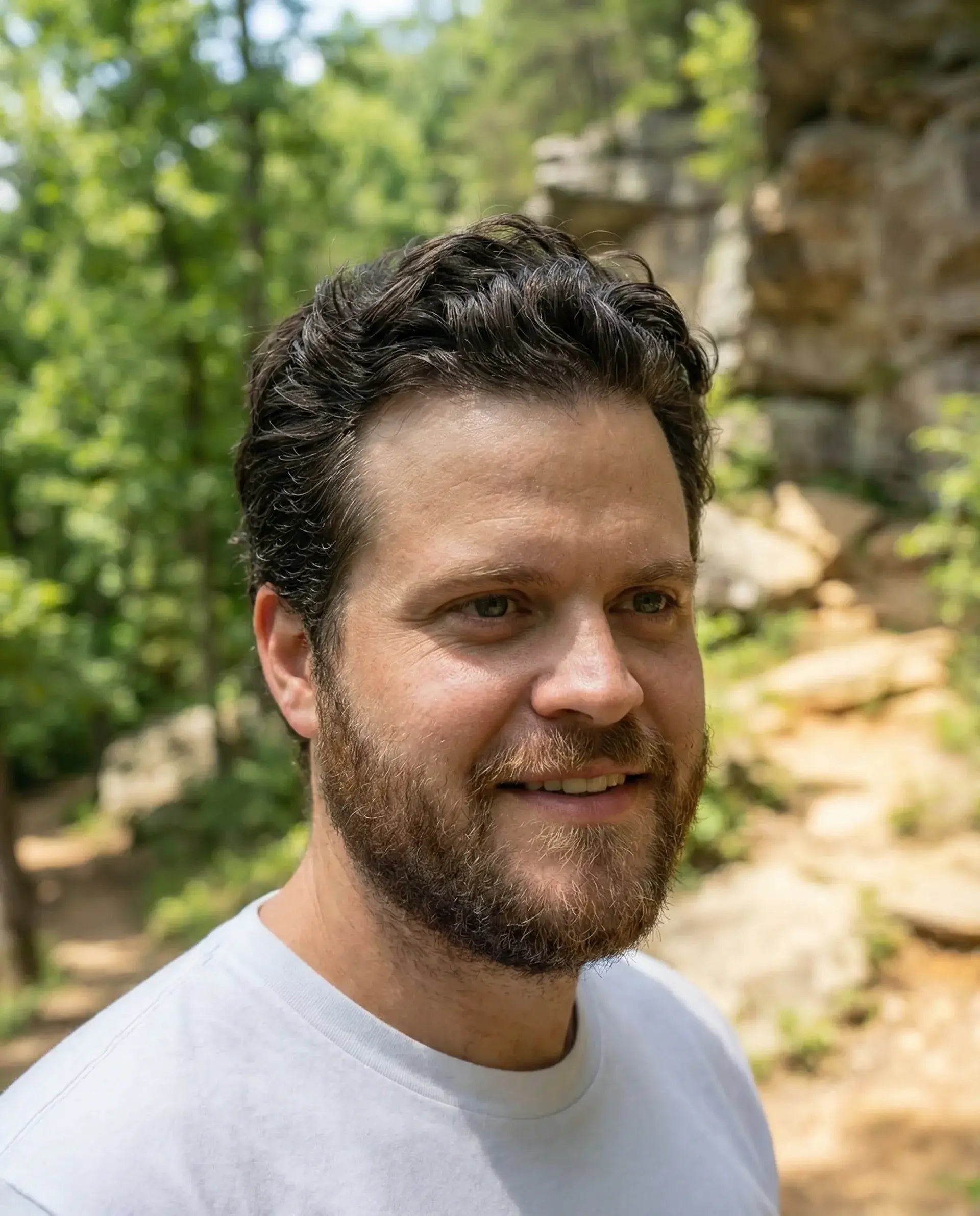 Man with a beard and short hair with greenery and rocks in the background showing off strong healthy hair after using Happy Lad's natural shampoo.