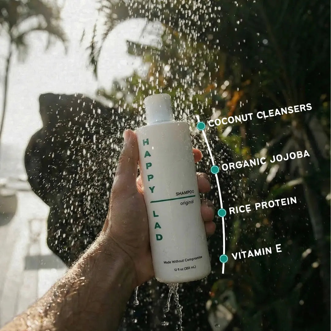 Hand holding a bottle of 'Happy Lad' natural shampoo for men under running water with product features highlighted.