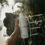 Hand holding a bottle of 'Happy Lad' natural shampoo for men under running water with product features highlighted.