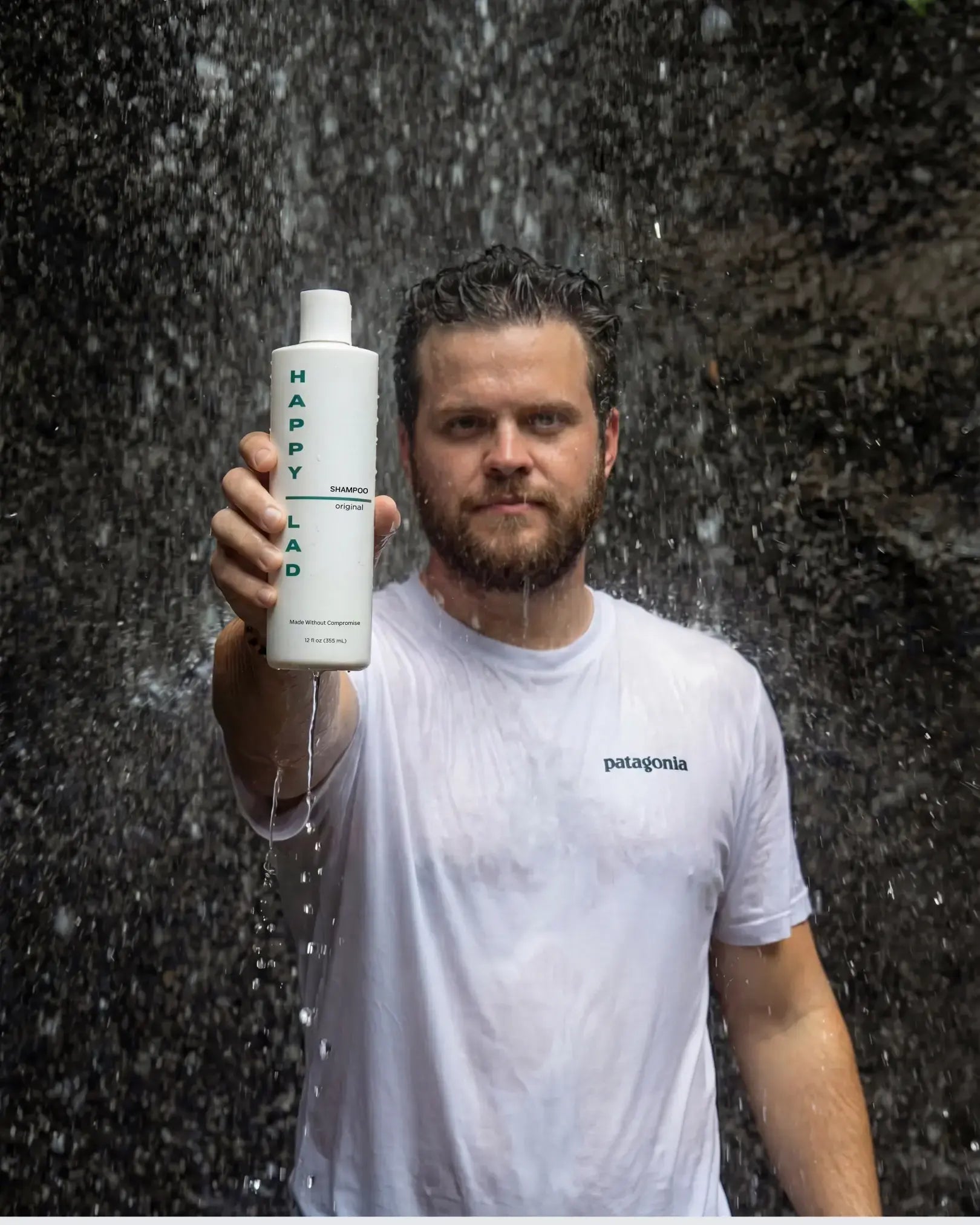 Man holding a bottle of mens natural non irritating shampoo for dry scalps from Happy Lad under a waterfall.