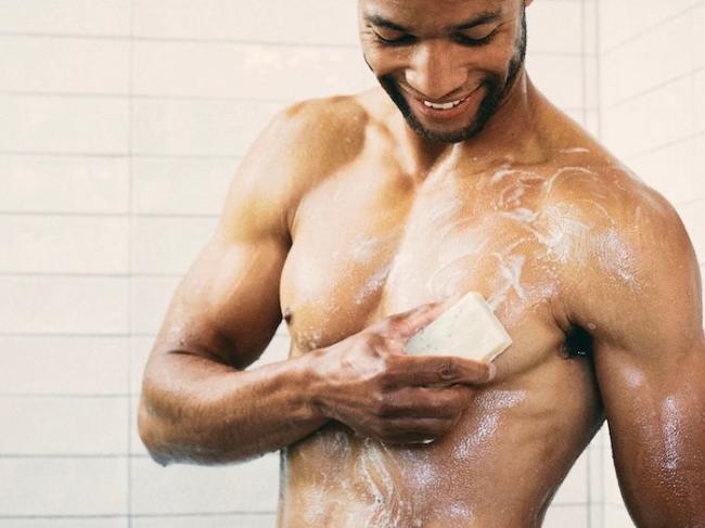 Smiling man washing body with a men's natural bar soap that creates good lather - made with organic ingredients.