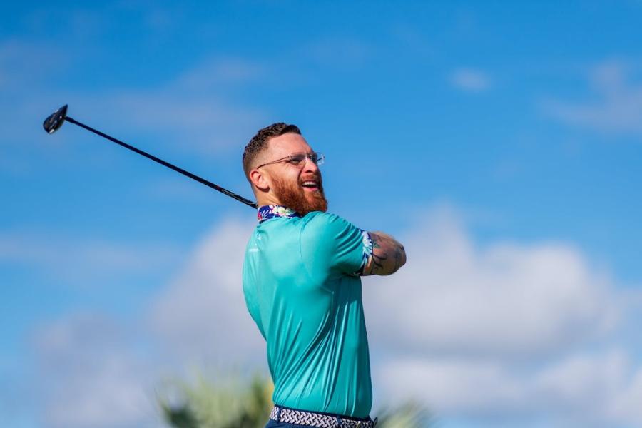 A smiling man swinging a golf club during a beautiful day.