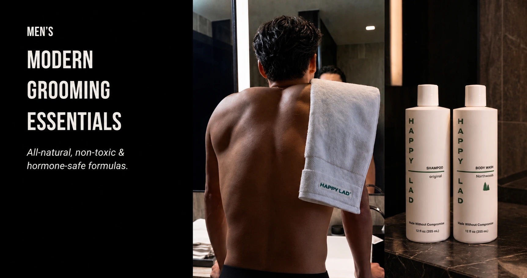 A shirtless man stands looking in mirror with a Happy Lad towel draped over his shoulder. Happy Lad's Organic Body Wash for men and Natural Shampoo are on a marble table next to him.
