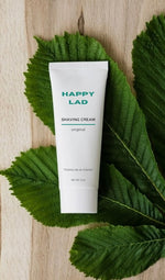 Happy Lad's natural shaving cream is set on a natural green plant.